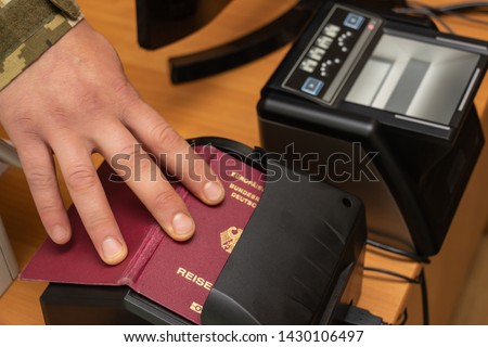 The process of scanning a German biometric passport to register the fact of crossing the state border. Male hand applies a passport to the scanning device. Concept of overseas travel Royalty-Free Stock Photo #1430106497
