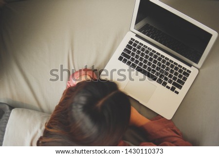 Top view of young woman comfortably using laptop in bed.