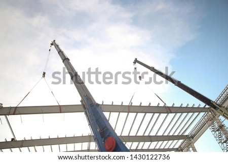 Mobile cranes are lifting steel roof structures in the construction area.