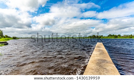 Dock platform on River Shannon with a slight swell in water, buildings, green vegetation and horizon in background, wonderful spring day in County Westmeath, Ireland
