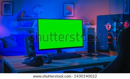 Powerful Personal Computer Gamer Rig with Mock Up Green Screen Monitor Stands on the Table at Home. Cozy Room with Modern Design is Lit with Blue and Neon Light.