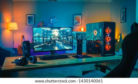 Powerful Personal Computer Gamer Rig with First-Person Shooter Game on Screen. Monitor Stands on the Table at Home. Cozy Room with Modern Design is Lit with Warm and Neon Light. Royalty-Free Stock Photo #1430140061