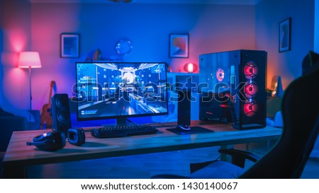 Powerful Personal Computer Gamer Rig with First-Person Shooter Game on Screen. Monitor Stands on the Table at Home. Cozy Room with Modern Design is Lit with Pink Neon Light. Royalty-Free Stock Photo #1430140067