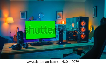 Powerful Personal Computer Gamer Rig with Mock Up Green Screen Monitor Stands on the Table at Home. Cozy Room with Modern Design is Lit with Warm and Neon Light.
