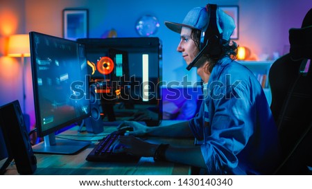 Professional Gamer Playing First-Person Shooter Online Video Game on His Powerful Personal Computer. Room and PC have Colorful Neon Led Lights. Young Man is Wearing a Cap. Cozy Evening at Home. Royalty-Free Stock Photo #1430140340