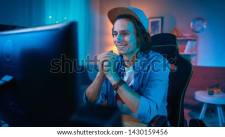 Handsome Excited Young Man Watching an Action Video on a Computer. He is Happy. Cozy Room is Lit with Warm Light.