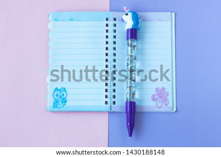School stationery with stylish unicorn pen on a pink and purple duotone background. Notebook with lines. Back to school creative table desk, flatlay and top view, copy space.