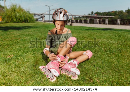 Teenage girl in a helmet learns to ride on roller skates holding a balance or rollerblading and spin at the city's street in sunny summer day. Healthy lifestyle, childhood, hobby, leisure activity.