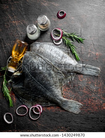 Raw fish flounder with rosemary, spices and onion rings. On dark rustic background