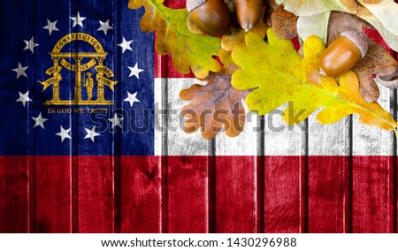State of Georgia flag on autumn wooden background with leaves and good place for your text.