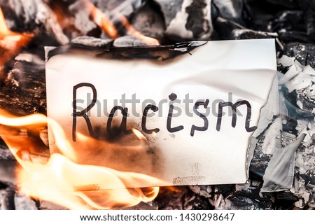 White paper with text of racism burning in fire. The concept of racism. Discrimination, racial problems Royalty-Free Stock Photo #1430298647