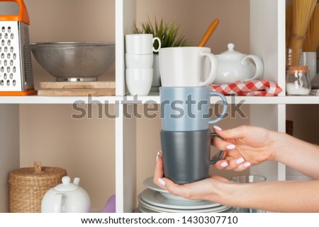 Woman hand taking dishware pieces from shelf in kitchen
