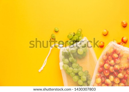 Eco bags with grapes and cherry on color background