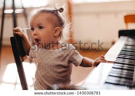 Cute little happy child girl playing piano in a light room. Selective focus, noise effect