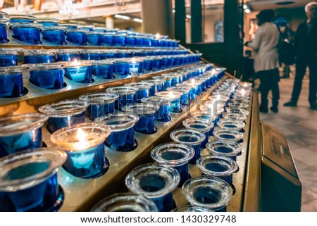 A series of devotional tea light candles arranged on a stand. Low-light image with people in the background (blurred out). These tea light arrangements are commonly seen inside churches.