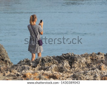 A woman dressed in a fashionable dress makes a photo during sunset on a rocky shore against the background of the Atlantic Ocean. back view.