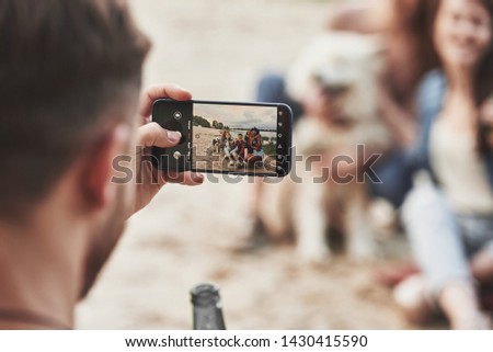 Using smartphone. Group of people have picnic on the beach. Friends have fun at weekend time.