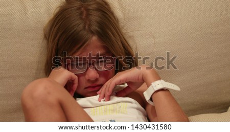 Little girl wearing reading glasses seated on couch watching scary movie.