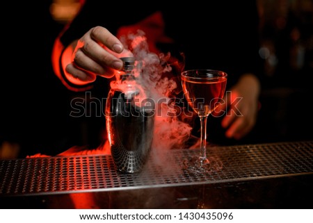 Close-up of steaming stainless steel shaker and refreshing cocktail on metal bar counter