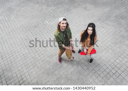 high angle view of beautiful woman and man standing with skateboards, looking at camera