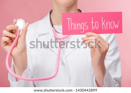 partial view of doctor in white coat and stethoscope holding card with things to know lettering isolated on pink