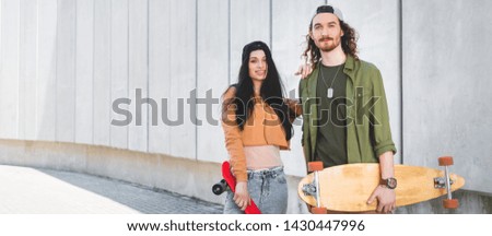 panoramic view of happy woman in casual wear putting hand on man, standing near concrete wall with skateboards
