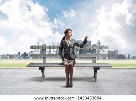 Business woman taking selfie photo or chatting with smartphone. Attractive girl using mobile phone on wooden bench. Mobile marketing and communication. Modern cityline panorama in sunny day
