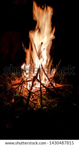 A  nighttime picture taken of a  campfire  burning hot with tall flames.  Sticks and limbs can be seen in the flames with a dark night background. 