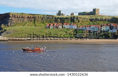 Whitby harbour, Yorkshire, UK. An old lifeboat now used as a pleasure craft, leaves harbour carrying passengers on a short sea trip. Whitby Abbey can be seen  high on a background cliff.