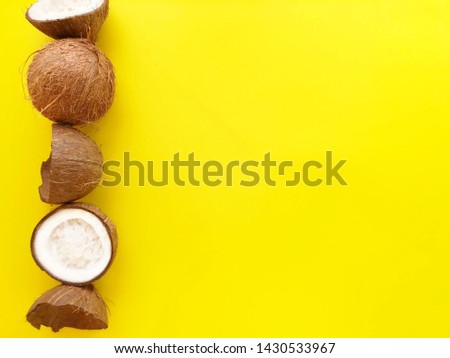 Creative layout of fresh ripe coconuts laid out in a row vertically on a bright yellow background. Summer concept. Top view, flat lay, copy space for text.