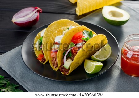 Appetizing hard-shell tacos with avocado, beef, tomato, cilantro and sour cream. Served with lime slices and jar of salsa sauce.