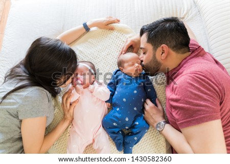High angle view of mom and dad kissing little twins while lying on bed
