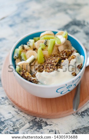 Greek yogurt, granola, kiwi and banana in bowl with a spoon on a gray concrete background, wooden tray, vertical format. Fitness diet for weight loss, proper and tasty food