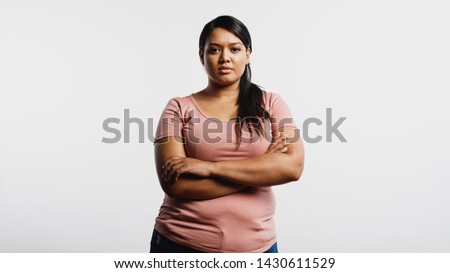 Woman with arms crossed standing against white background. Portrait of an obese woman looking at camera.