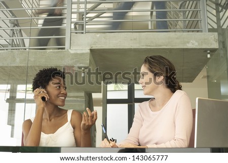 Young businesswoman on call with female colleague noting down at table