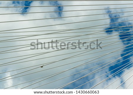 Lisbon's Vasco da Gama suspension bridge cables in detail against a cloudy sky.