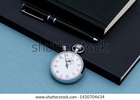 Black notebook, pencil and chronometer on the blue background.