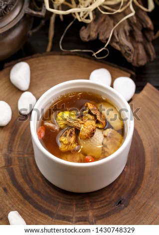 White broth in a white soup pot placed on a wooden chopping board
