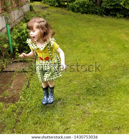 
Little girl having fun after the rain. The child jumps through the puddles in rubber boots.