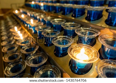 A series of devotional tea light candles arranged on a stand. Low-light image. Commonly seen inside churches.