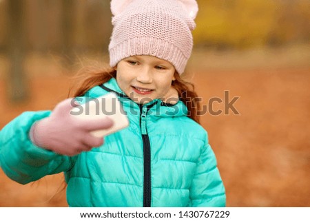 childhood, season and people concept - happy girl taking selfie by smartphone at autumn park