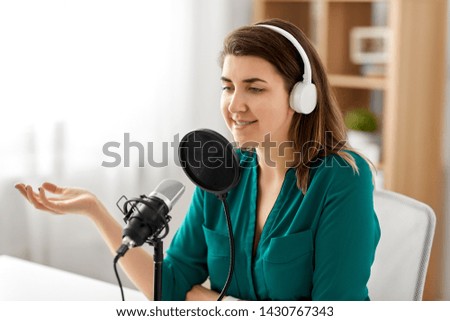 technology, mass media and people concept - woman with microphone and headphones talking and recording podcast at studio