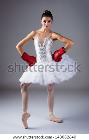 Beautiful female ballet dancer on a grey background. Ballerina is wearing a white tutu, pointe shoes and red boxing gloves.