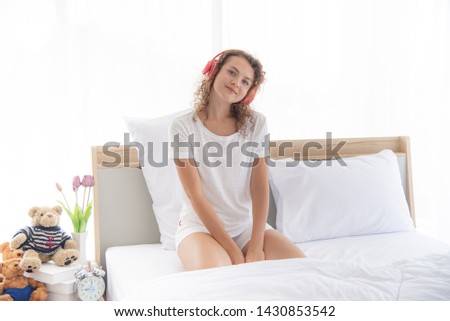 Caucasian young and beautiful woman with boring face or unhappy sitting on the  comfortable  double bed in modern or minimal interior bedroom design decorated with , white bedding and wooden furniture