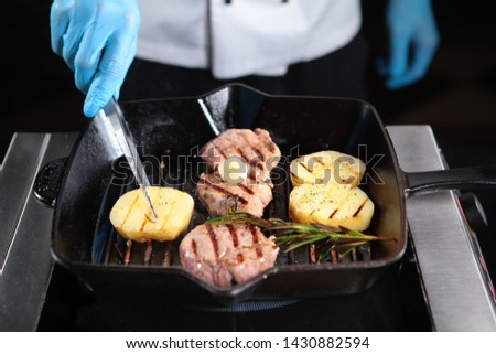 Cooking a piece of beef on the grill indoors. Cooks hands in the frame. Fillet of beef minion. Delicious dish of natural meat. Grilled vegetables in a pan.