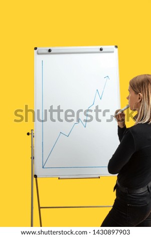 back view of businesswoman standing near white flipchart, looking at growth graphic, standing isolated on yellow