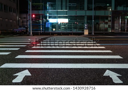 Pedestrian crossing with directional arrows at night. pedestrian marking on wet pavement. red signal for traffic lights. pedestrian crossing opposite business building