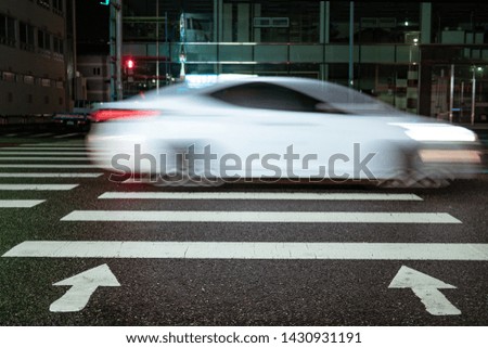white car quickly drives through the pedestrian zebra. Pedestrian crossing with directional arrows at night. pedestrian marking on wet pavement. red signal for traffic lights.