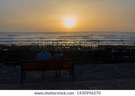 Elderly people sit and watch the sunset by the sea. The concept of eternal love.