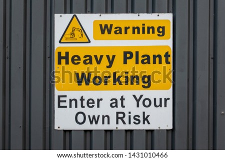 Warning heavy plant working enter at your own risk sign on the side of an industrial unit
